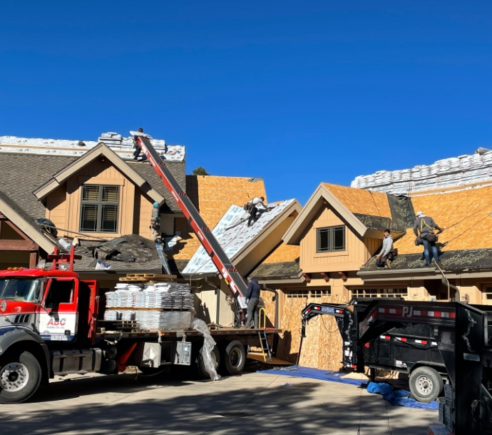 Active roofing installation with workers on the roof and a boom truck lifting materials, with a clear blue sky above, showcasing the process and equipment involved in residential roofing projects.
