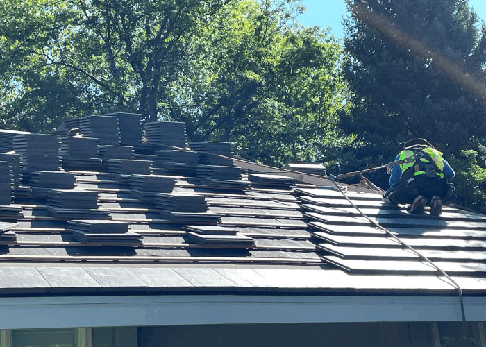 Roofing professional installing clay tiles on a residential roof with safety harness in place, amidst lush greenery.