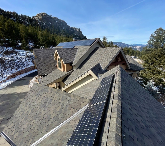 Sophisticated mountain home with asphalt shingle roofing and solar panels, set against a scenic backdrop of snowy hills and evergreens, blending eco-friendly energy with rustic architecture.