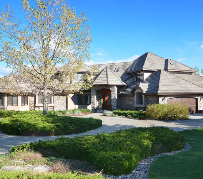 Luxurious stone-front home with multiple gabled roofs and a curved driveway set amidst manicured landscaping, conveying a sense of grandeur and attention to detail in residential design.