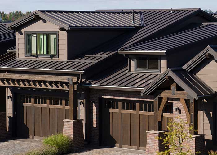 Modern home featuring a dark metal roof with clean lines, snow guards, and multiple gables, complemented by stone column details and wooden garage doors, reflecting contemporary architectural roofing trends.