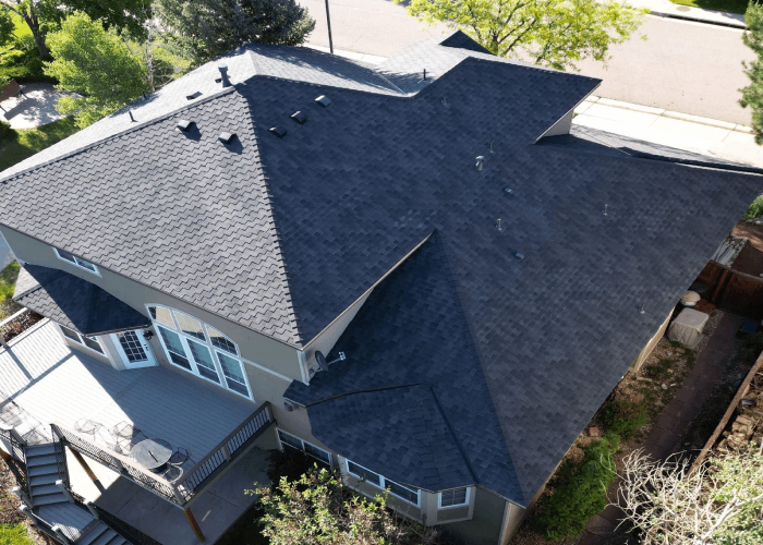 Aerial view of a home showcasing a newly installed asphalt shingle roof with complex angles and ridge vents, emphasizing modern roofing design and efficient ventilation systems for enhanced home comfort.
