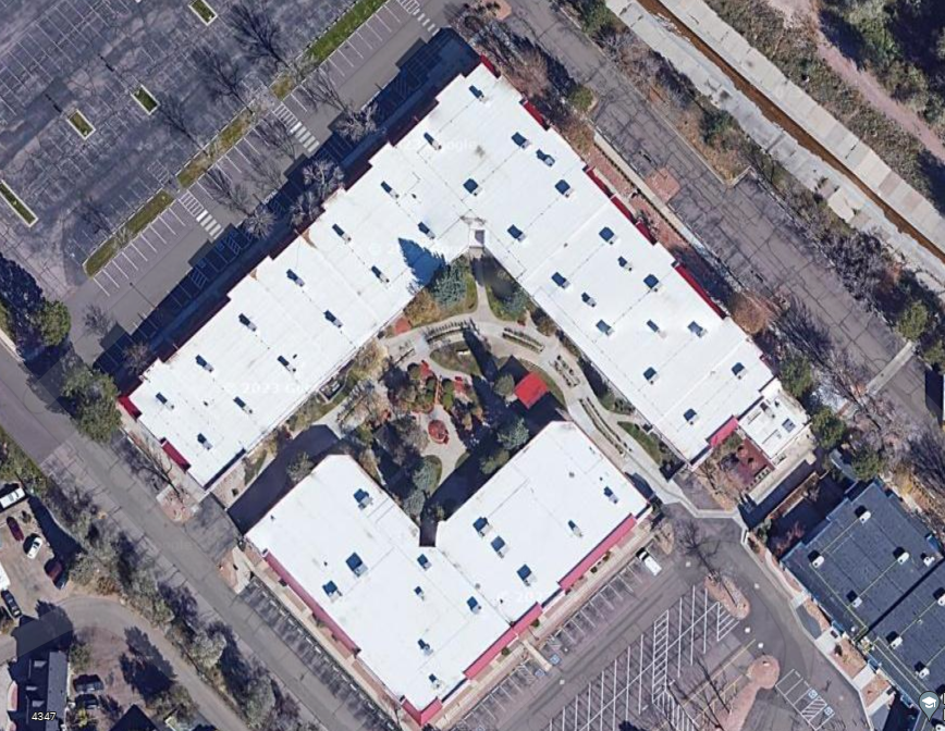 Aerial view of a commercial complex with multiple flat-roofed buildings and an adjacent parking lot, showcasing typical urban planning and architecture in a densely built area