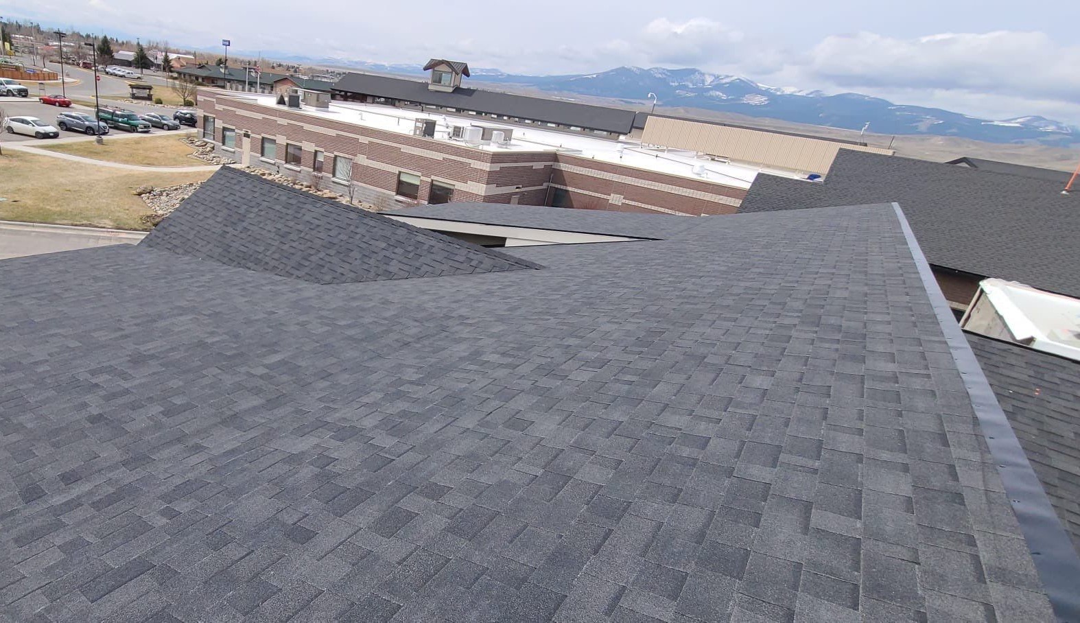 Expansive view of a complex commercial roof with architectural shingles, featuring the majestic mountain landscape in the background, highlighting a blend of functional design and natural beauty.