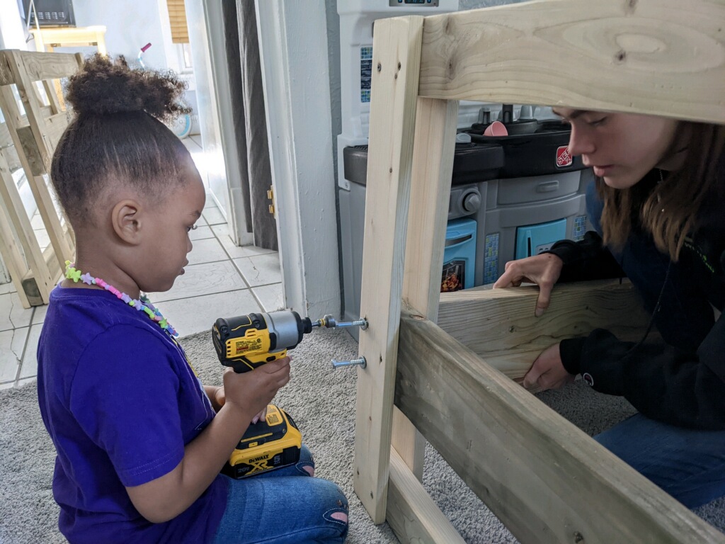 A young girl drilling a bolt into a walkway with the help of an adult