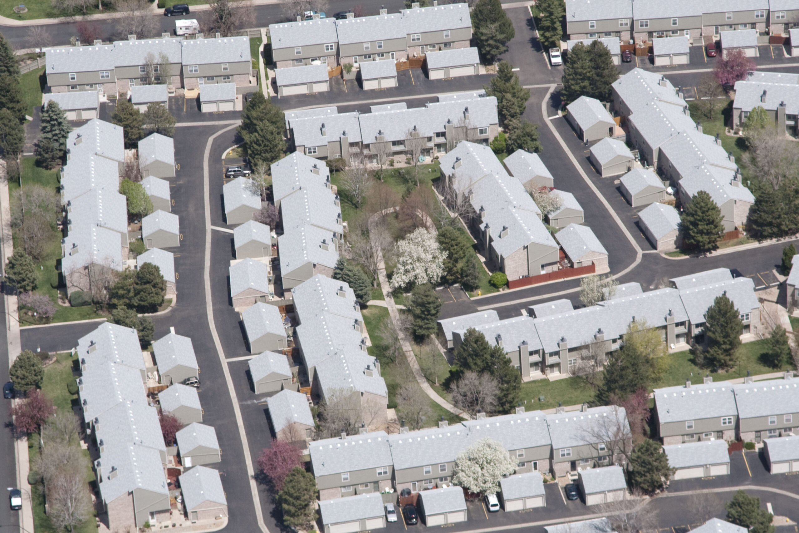Aerial view of a suburban area with uniform houses featuring white roofs, arranged in a neat grid pattern with interspersed greenery.
