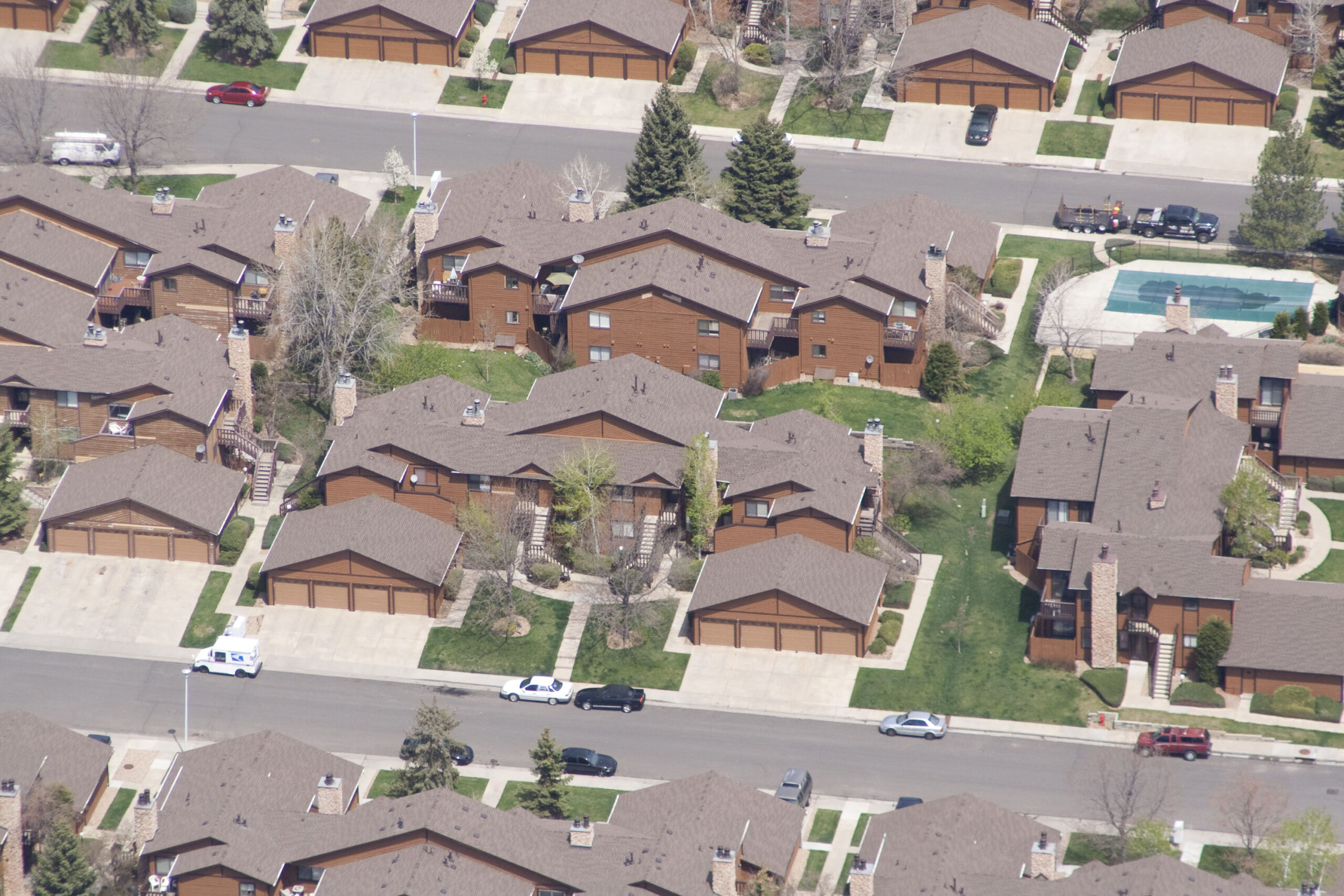 Aerial view of a suburban neighborhood showing a pattern of houses with brown roofs, neatly aligned along curving streets.