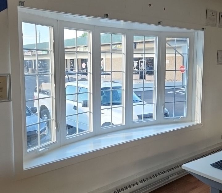 A large white-framed bay window with clear glass panes overlooks a parking area, allowing ample natural light into the room.