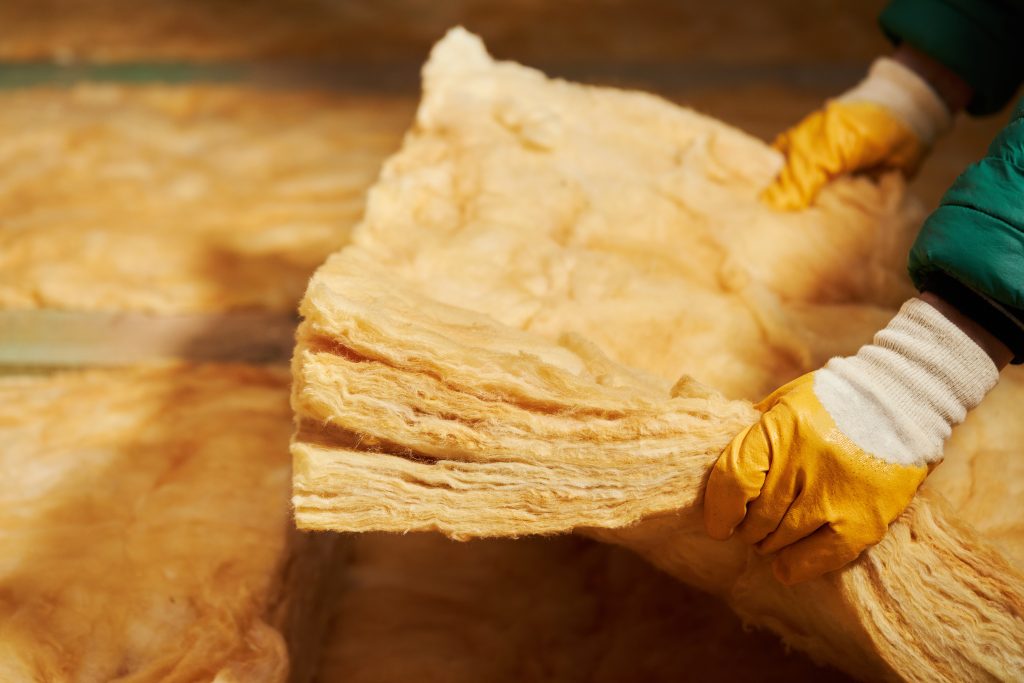 Construction worker thermally insulating house attic to decrease chances of getting ice dams on roof