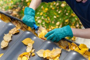 A man taking autumn leaves out of gutters for gutter cleaning and repair