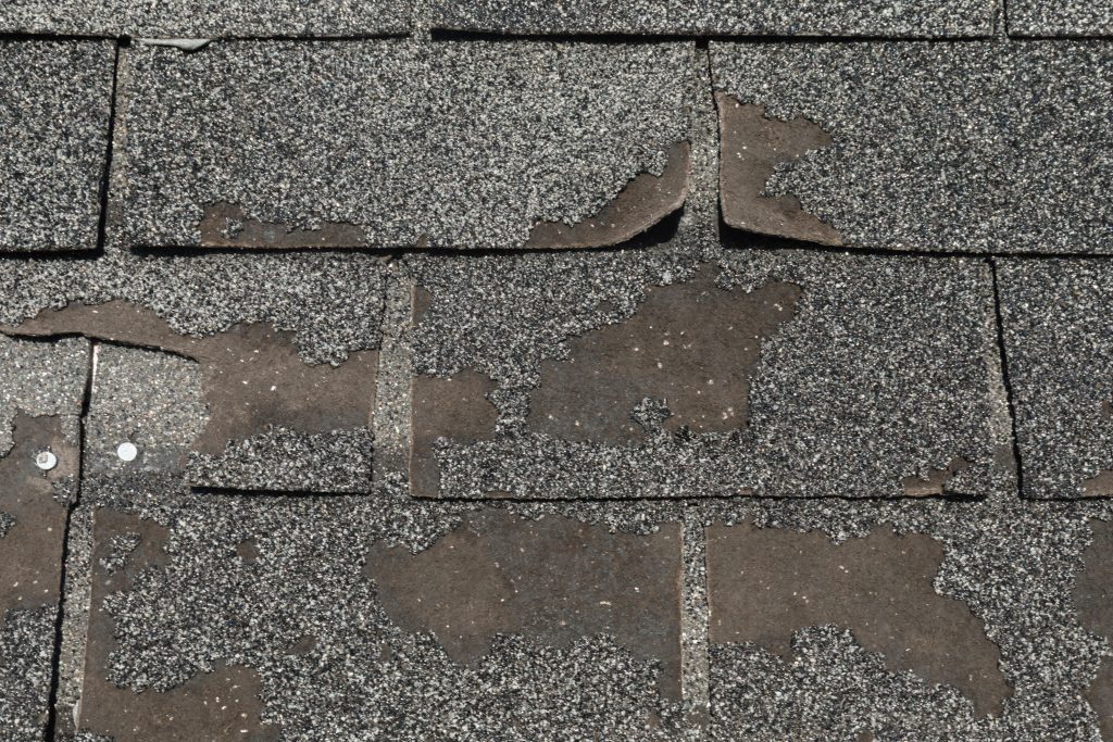 Roof in need of repair damaged asphalt roofing shingles. Broken worn asphalt roofing shingles 