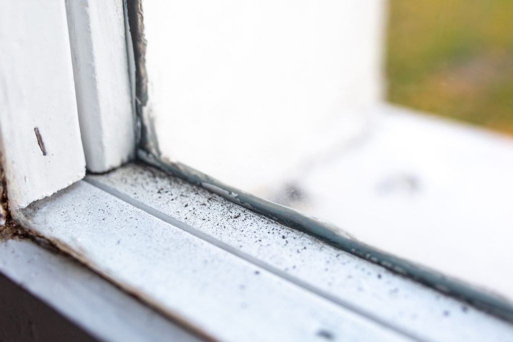 Dirty dust piled up inside of a window frame with a visible window seal failure