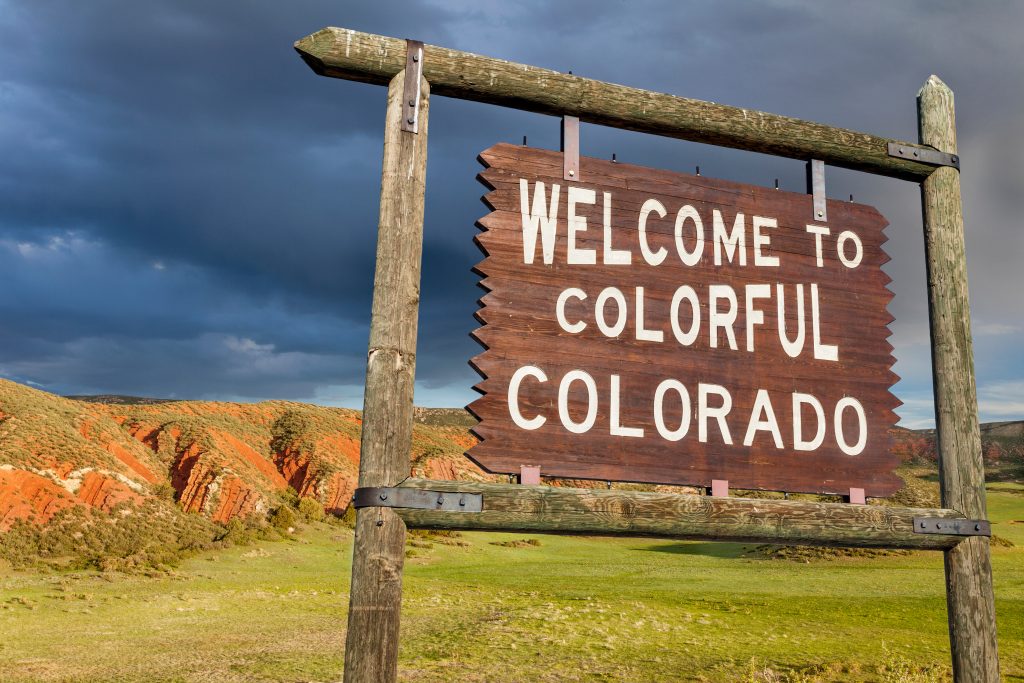 welcome to colorful Colorado roadside wooden sign with red sandstone cliff in background